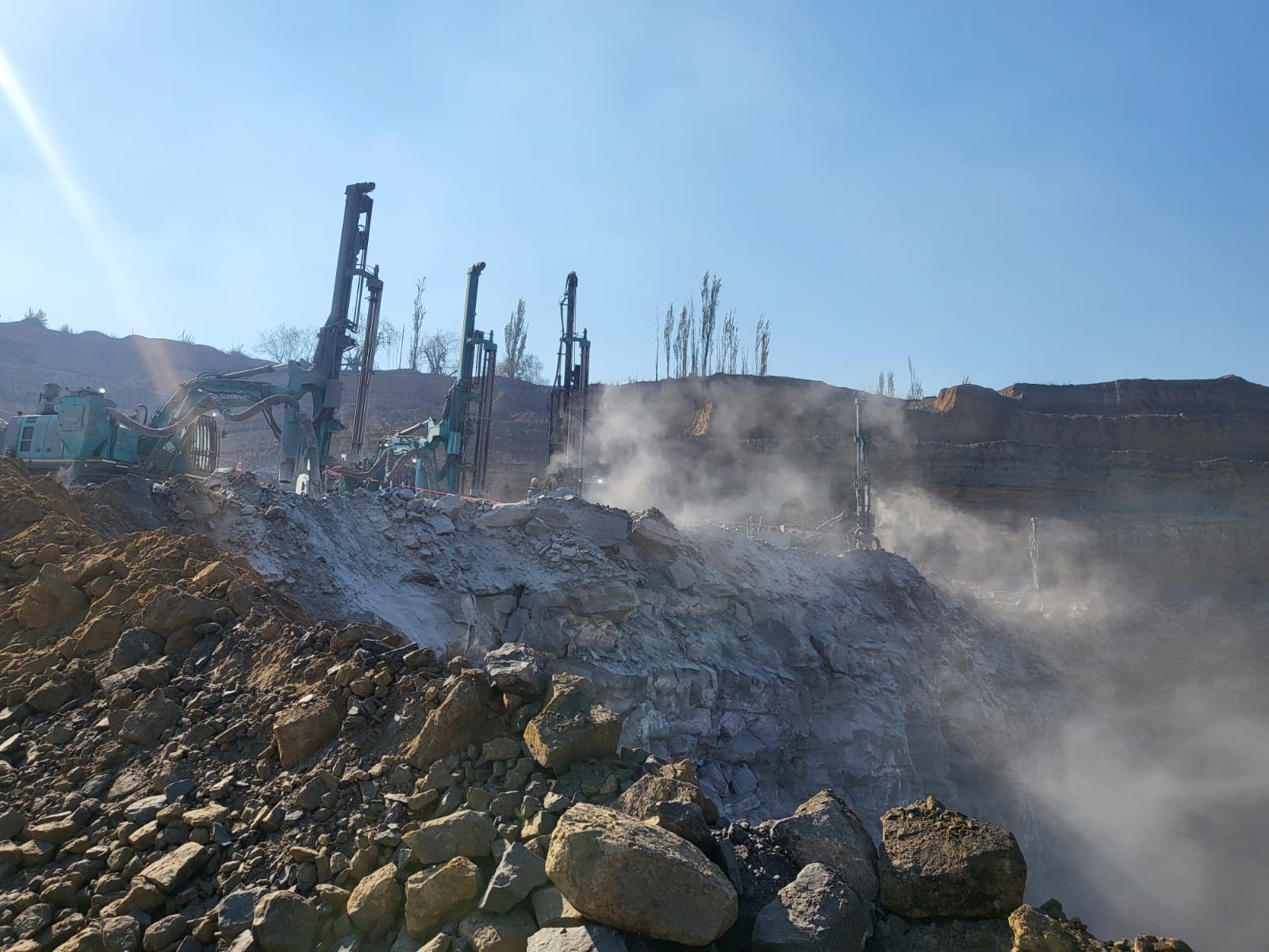 Drill rigs working a dusty bench with visible dust suppression conditions