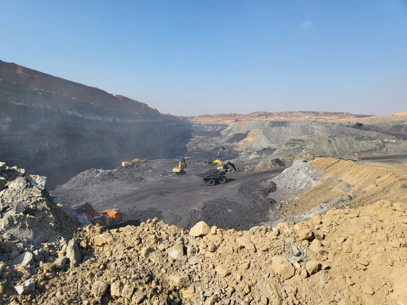 Panoramic view of an open-pit coal operation with excavators and haul trucks on the seam floor